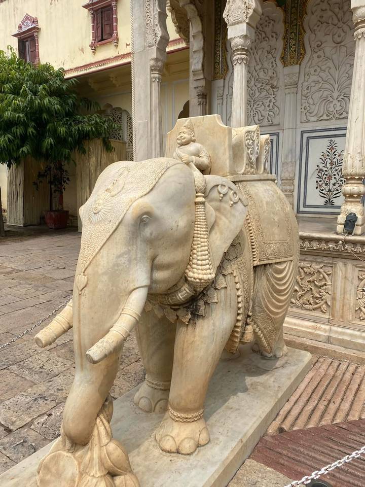 A finely carved marble elephant statue stands outside a historic palace courtyard.