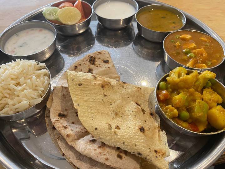 An Indian thali with rice, chapati, curries, and chutneys served on a metal tray.