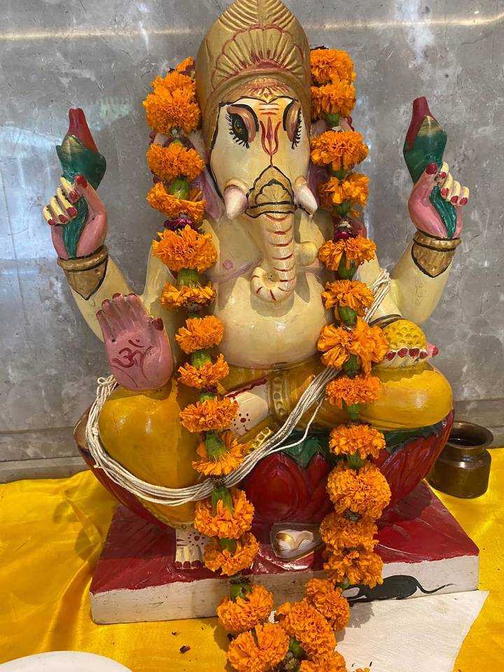 A colorful Ganesha statue adorned with fresh marigold garlands on a marble background.