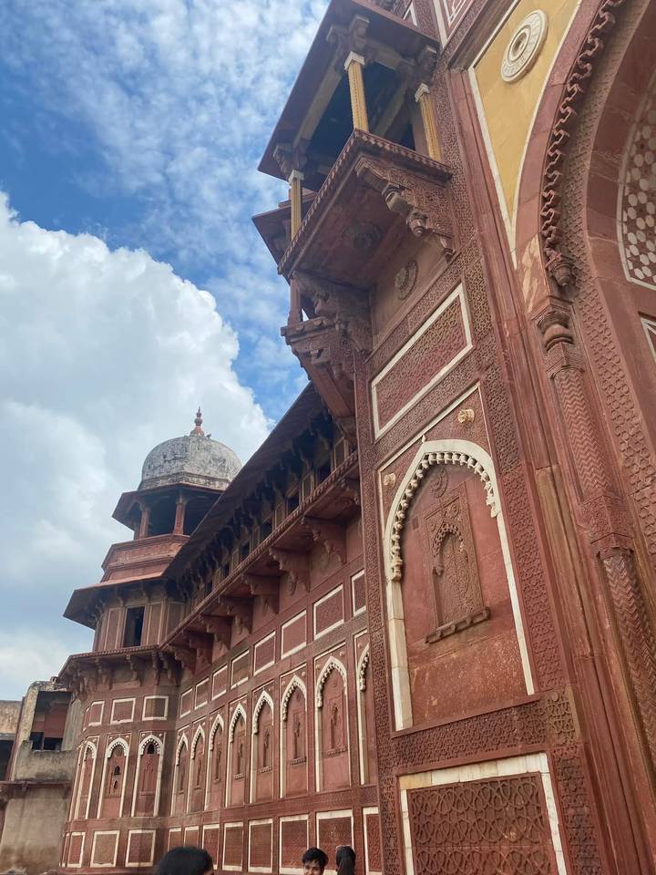 A towering red-sandstone façade with decorative arches and a dome set against a bright blue sky.