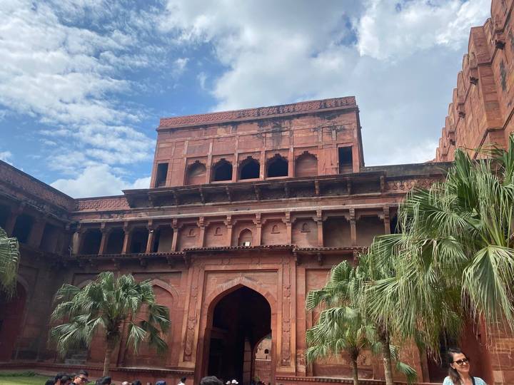 An inner courtyard façade of red-sandstone arches and balconies set against a cloudy sky.