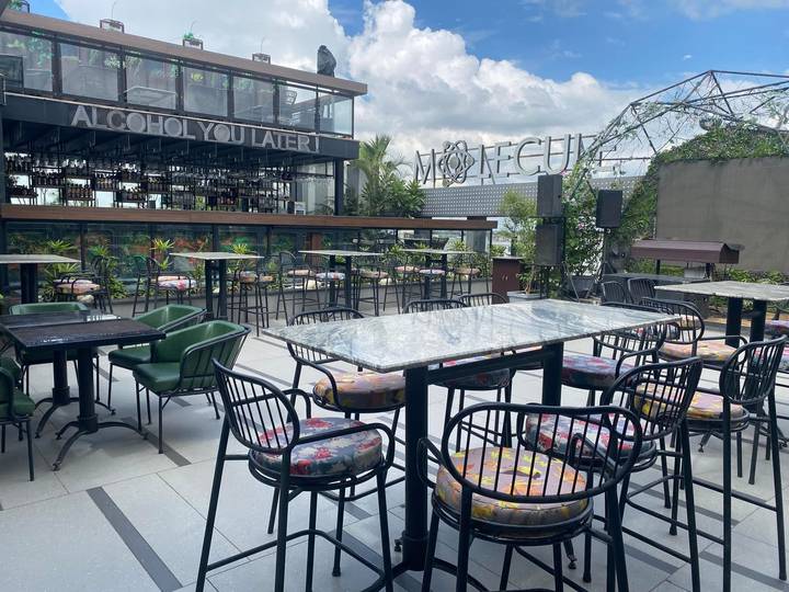 A chic rooftop bar with modern tables, colorful cushions, and a city skyline backdrop.
