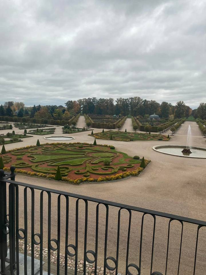 Formal baroque gardens with symmetrical hedges, fountains, and tree-lined alleys viewed from a terrace.