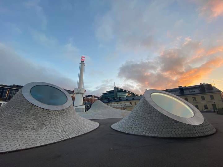 Futuristic skylight cones and flag column set against a colorful sunset sky.