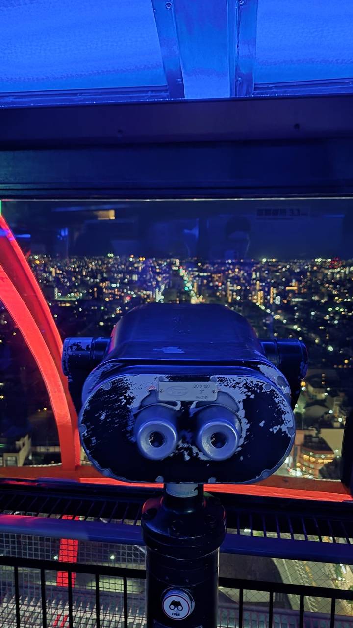 Night view of a sprawling city full of lights seen through an observation viewer inside a ferris-wheel capsule.