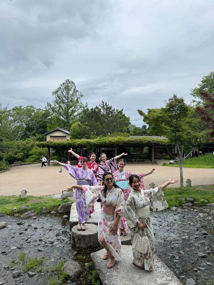 Group of women in colorful yukata pose happily in a Japanese garden courtyard with lush greenery.