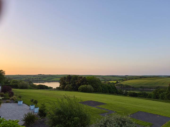 Gentle Irish countryside at dusk with river, rolling fields, and pastel sky.
