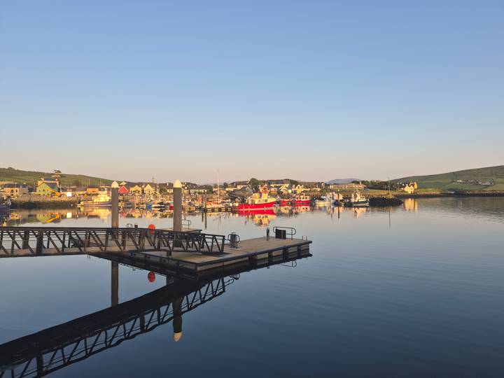 Calm morning reflection of boats and village at Dingle harbor.