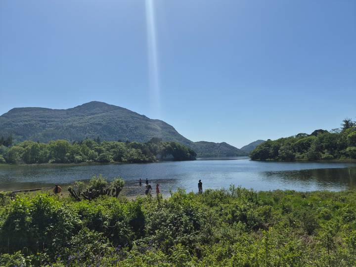 Lake in Killarney National Park with swimmers and forested mountains under clear sky.