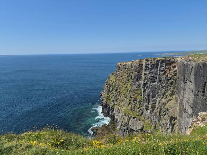 Dramatic sheer sea cliffs plunging into deep blue Atlantic waters under a clear sky.