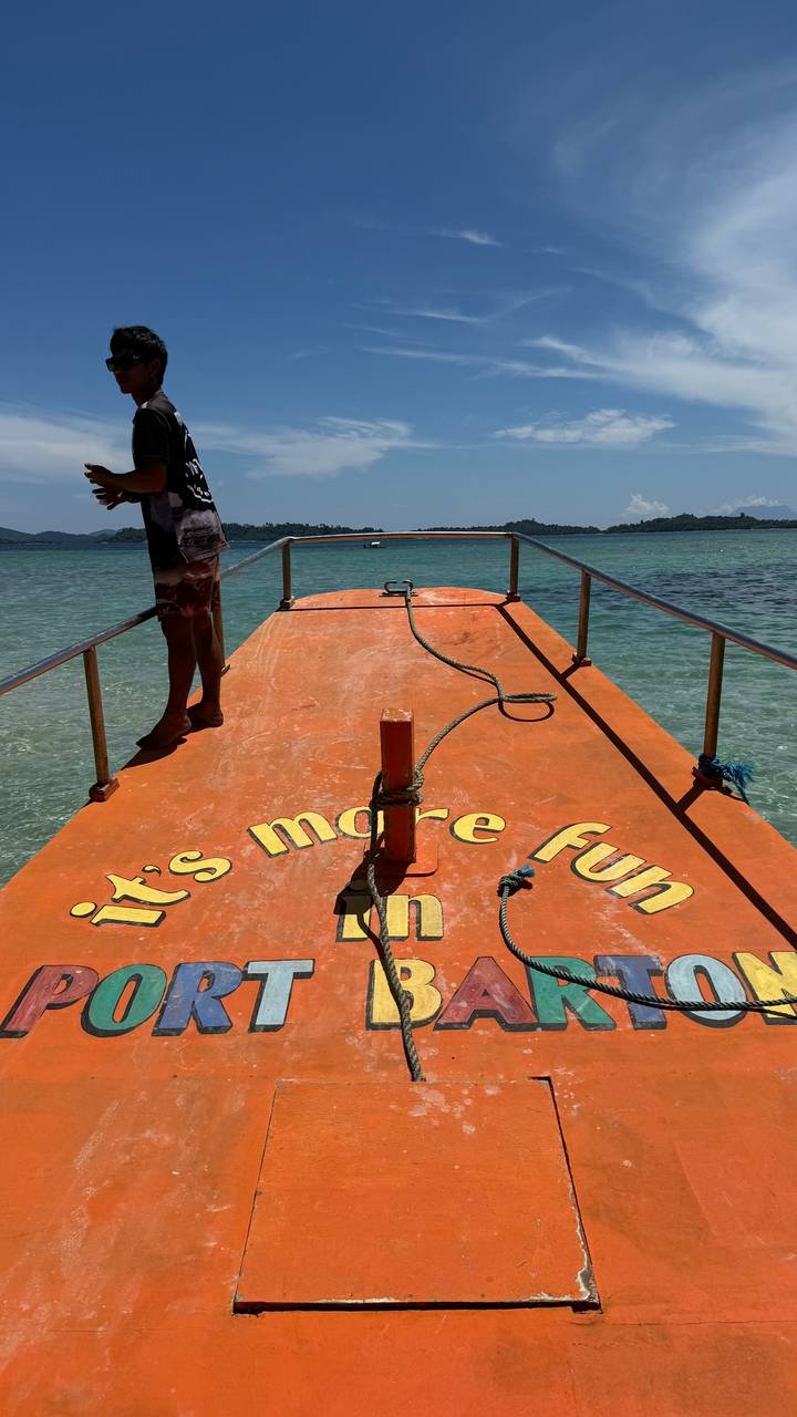 Bow deck of orange tour boat with slogan, clear aqua water and distant islands under bright sun.