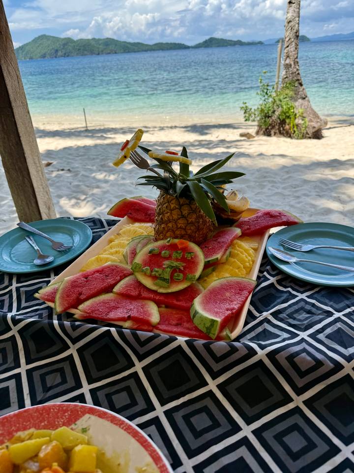 Colorful fruit platter on a beach hut table featuring watermelon carved with 'I ❤️ Port Barton' around a pineapple centrepiece.