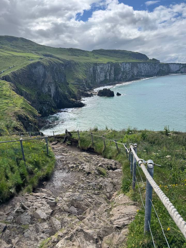 Coastal trail descending toward a rocky cove with safety fence alongside