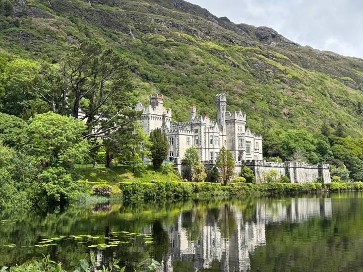 Victorian-era castle reflected perfectly in still lake amid green hills