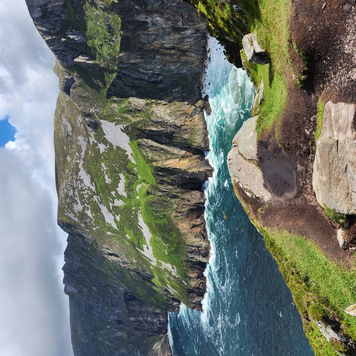 Dramatic sea cliffs with green slopes dropping into turquoise Atlantic waters