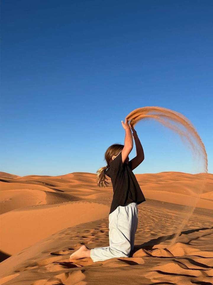 Child joyfully tossing an arc of desert sand high into the blue sky