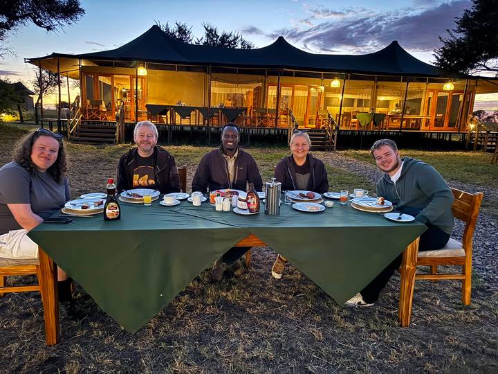 Travel group enjoying outdoor breakfast at safari camp at dawn