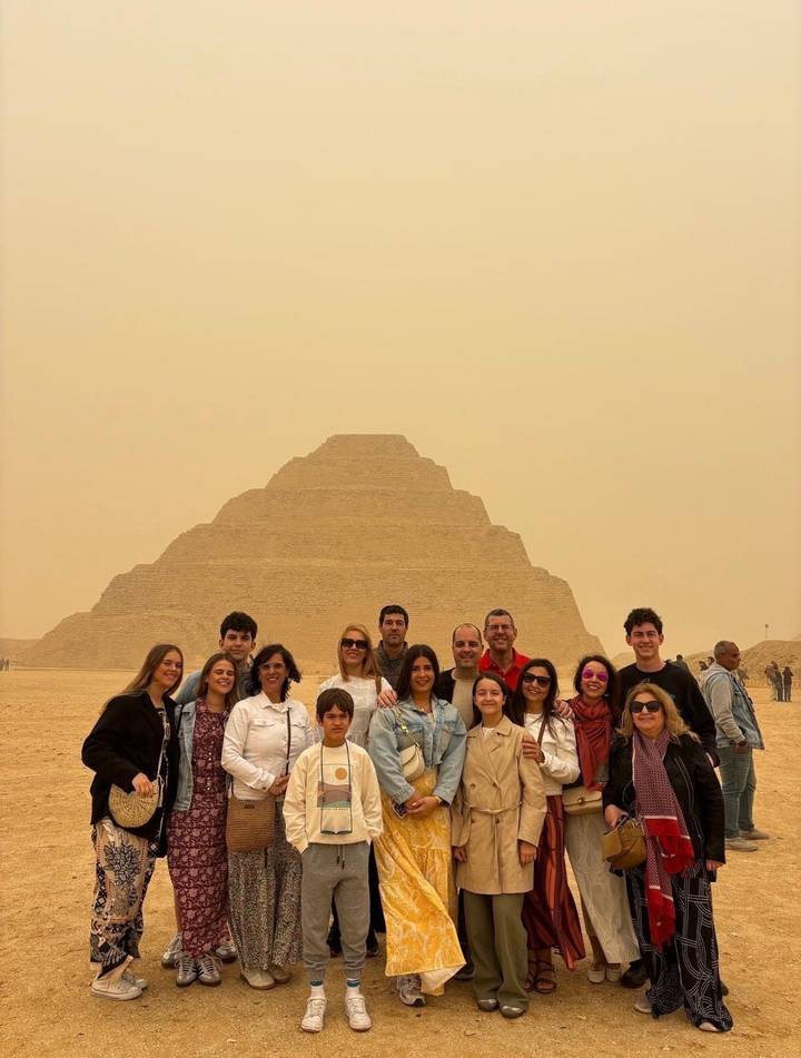Large tour group posing in front of the Step Pyramid of Djoser in a sandy, hazy desert setting.