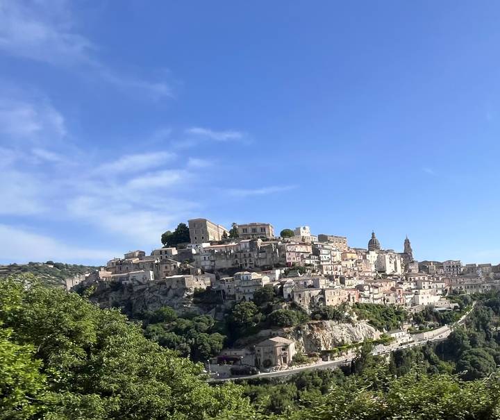 Panoramic view of the hilltop baroque town of Ragusa Ibla under a bright blue sky.