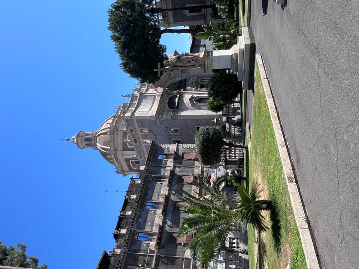 Baroque cathedral dome rising above Catania’s historic center with palm trees in front.