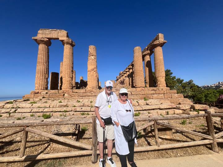 Smiling couple posing in front of ruined Greek temples at Agrigento under clear skies.