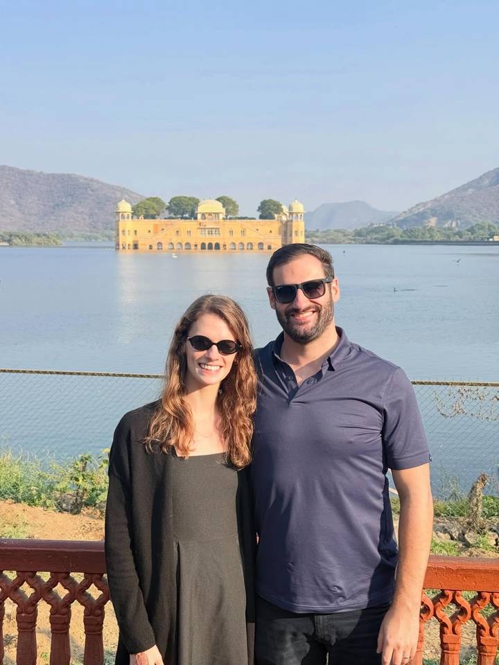 Couple posing beside Jaipur’s lakeside Jal Mahal palace with Aravalli hills in background.