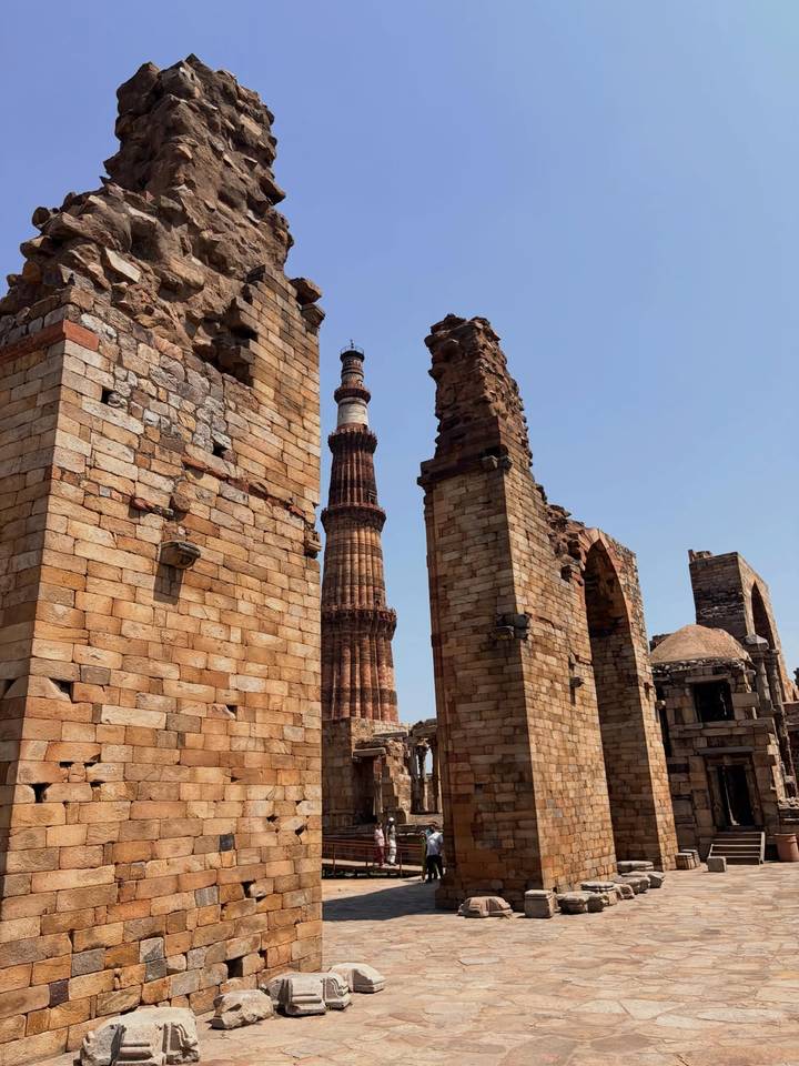 Stone ruins and the towering Qutub Minar framed by ancient arches in Delhi.