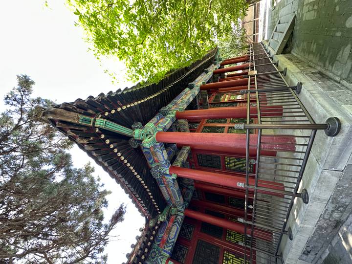 Colorful wooden pavilion with red pillars and painted eaves nestled among trees in Beijing.