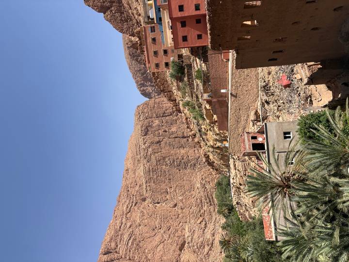Rocky red canyon walls and scattered village houses under a cloudless sky in Todra Gorge.