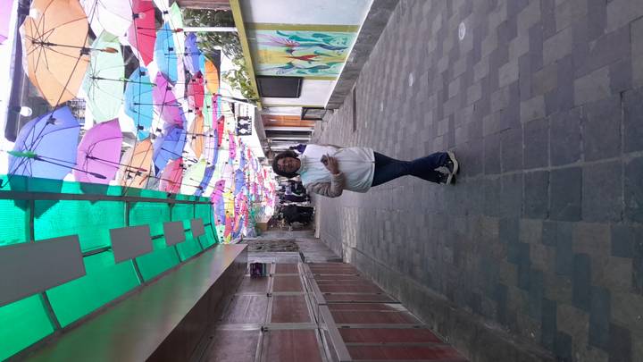 Woman poses in a narrow alley topped with rows of colorful hanging umbrellas.