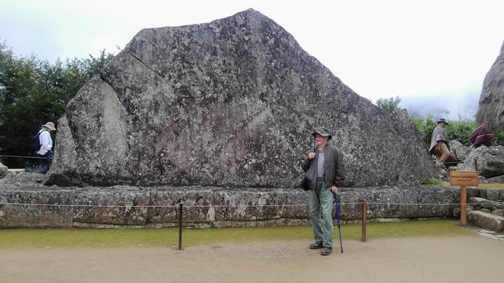 Visitor in hat stands beside a massive sacred stone inside the Machu Picchu archaeological site.