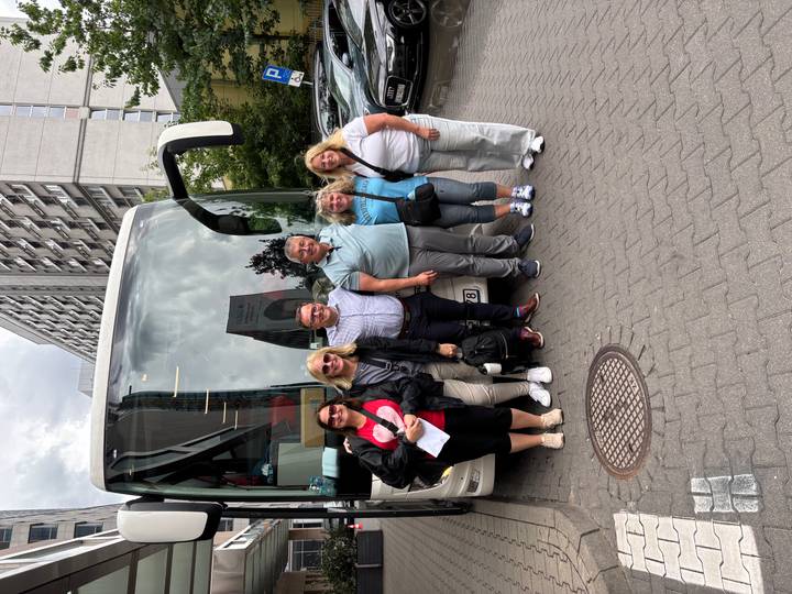 Group of tour participants stand beside their coach on a city street before departure.
