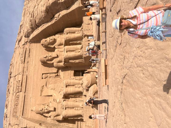 Visitors stand before the colossal seated statues of Abu Simbel carved into a sandstone cliff.