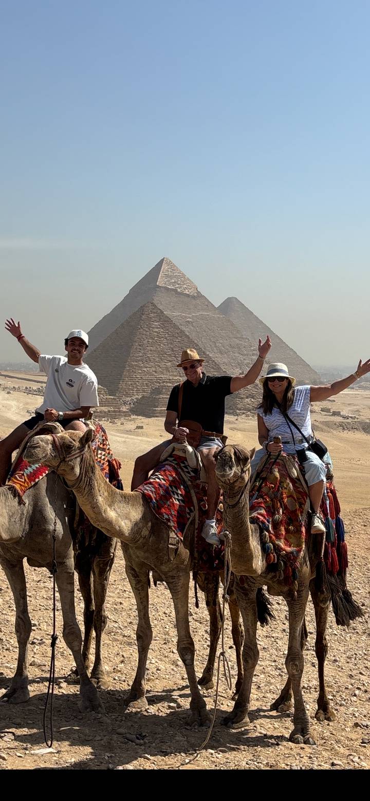 Family on camels pose with the pyramids rising behind them on the Giza Plateau.