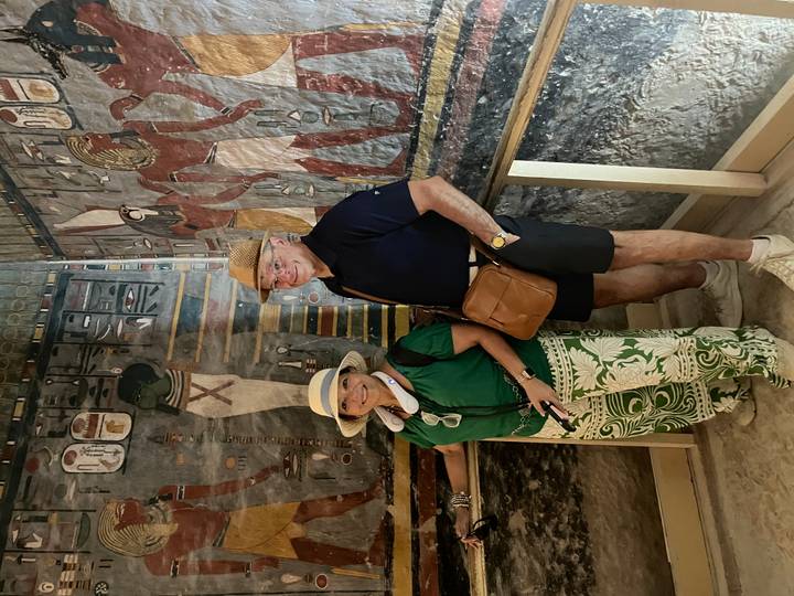 Tourists stand by rail inside a small painted chamber with ancient Egyptian figures on the walls.