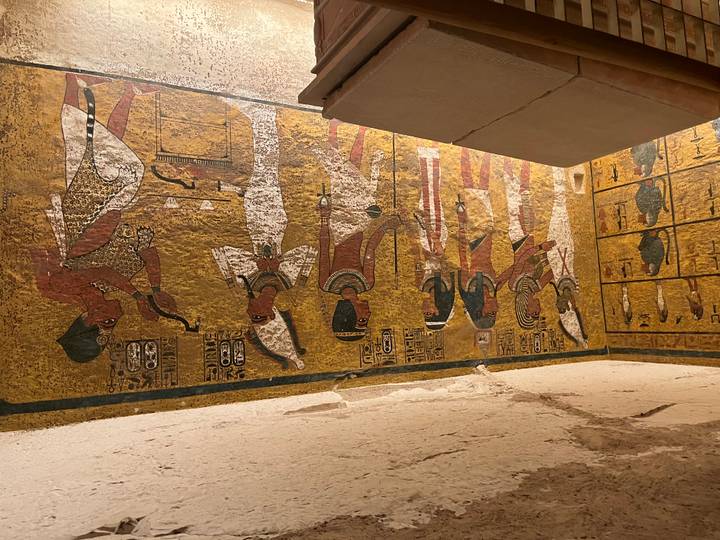 Wall of an Egyptian tomb featuring detailed scenes of deities and pharaohs painted on a golden background.
