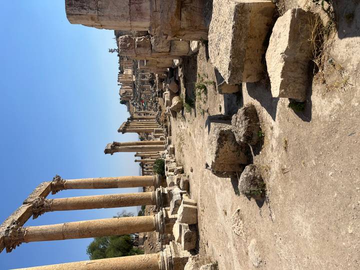 Ancient colonnaded Roman ruins with scattered stone blocks under a clear blue sky.