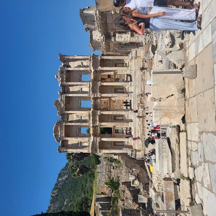 Front view of the Library of Celsus with visitors scattered on the steps under clear skies.
