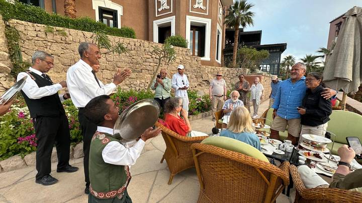 Tourists and local musicians gather on a hotel terrace for refreshments and music.