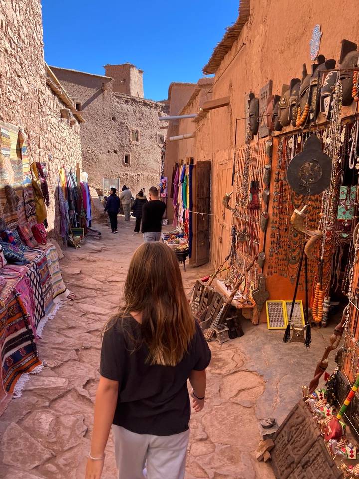 Narrow souk alley lined with colorful textiles and crafts in a Moroccan kasbah.