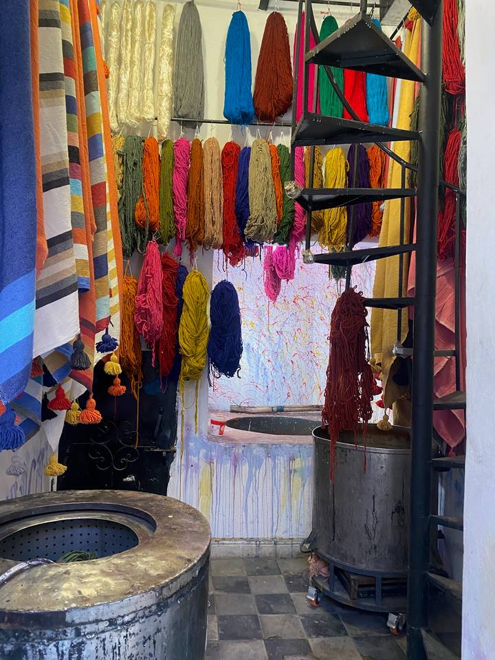 Bundles of brightly dyed wool hang from rafters in a Moroccan workshop.