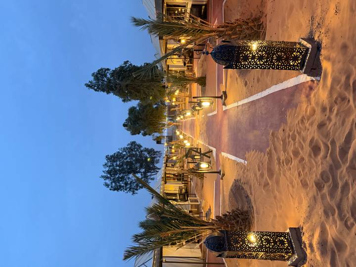 Evening view of a luxury desert camp walkway lit by lanterns under a blue twilight sky.