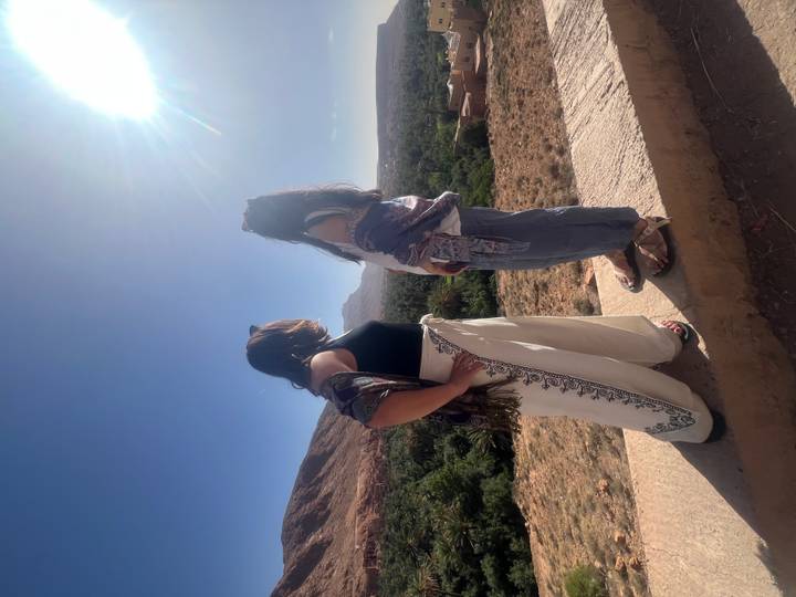 Two friends admire a sun-lit desert valley with palms while wrapped in scarves.