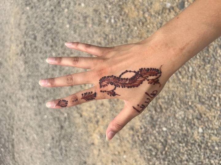 Hand decorated with fresh henna designs featuring Arabic script and leaves.