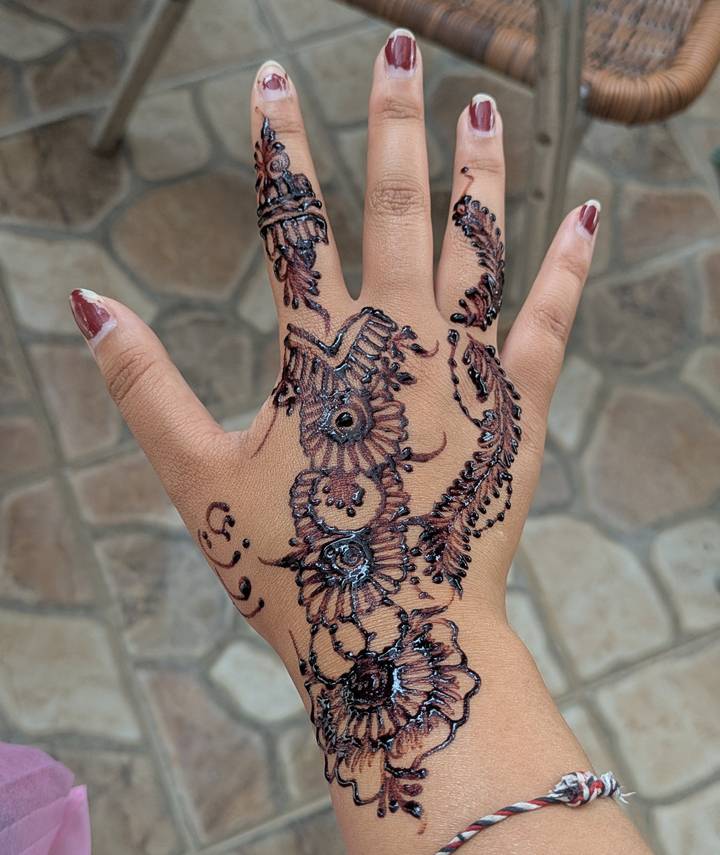 Freshly applied intricate black henna pattern on the back of a hand.