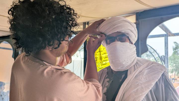 Local guide wraps a turban around a visitor inside a desert tent.