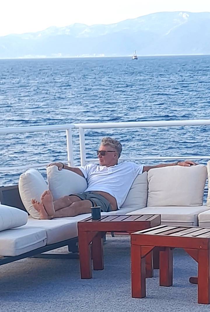 Man lounges on cushioned deck seating of a yacht with the Adriatic Sea beyond.