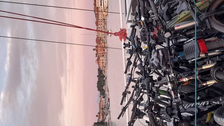 Dozens of bicycles stacked on the deck of a boat at pink sunset over a harbor.
