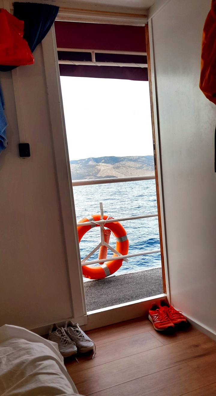 View through a cabin door to the open sea with an orange life buoy on the railing.