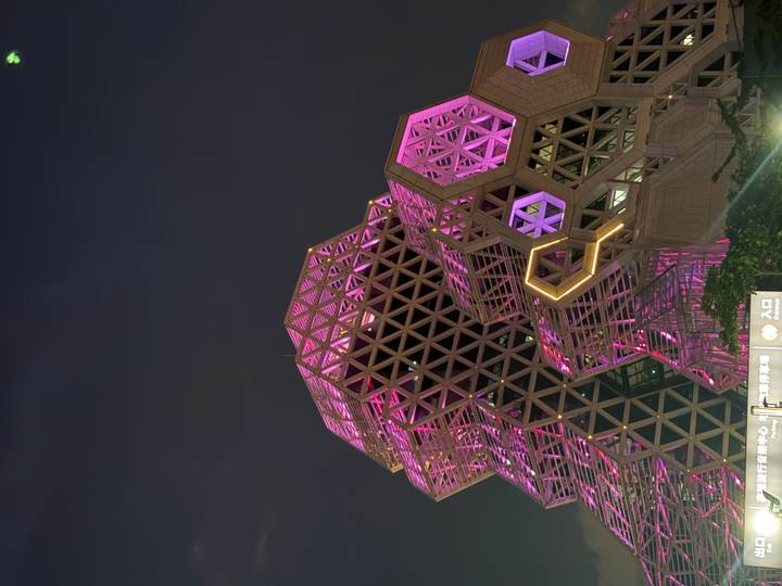 A striking modern hexagonal building lit with vivid pink and purple lights against the night sky.